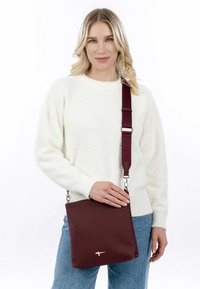 Tumepruun nahast õlakott minimalistliku disainiga, reguleeritava rihma ja metallist detailidega. Sile tekstuur, ruudukujuline.