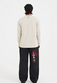 Hellgraues Langarmshirt, kombiniert mit schwarzen Hosen, die ein rotes Dolchgrafik und ein Flammendesign am linken Bein aufweisen. Lässige Passform.