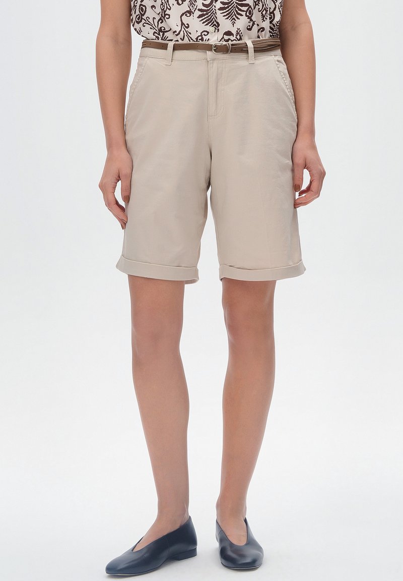 Beżowe szorty do kolan z podwiniętymi nogawkami, posiadające boczne kieszenie i gładką fakturę. W połączeniu z wzorzastą bluzką i czarnymi płaskimi butami.