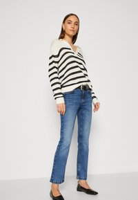 Stripet strikkegenser i krem og marineblå, v-halsdesign. Kombinert med blå jeans og svarte flate sko. Enkle tilbehør, avslappet passform.