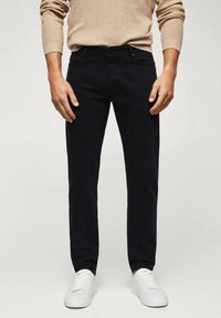 Jean slim bleu foncé en coton avec poches avant et arrière, associé à des baskets blanches et un pull beige texturé.