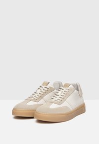 Zapatillas de ante y cuero beige con puntera redonda, paneles blancos y suela de goma. Presentan cordones beige y un logo sutil en la lengüeta.