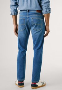 Jeans in denim azzurro chiaro, fit dritto con due tasche posteriori. Presentano cuciture gialle e una toppa in pelle marrone in vita.