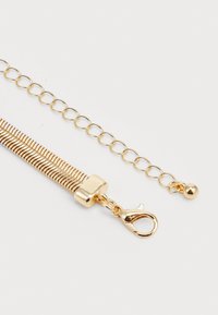Pulsera de cadena de oro con un diseño plano y acanalado, que incluye un cierre de langosta y una cadena ajustable para personalizar el tamaño.