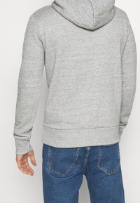 Grå hoodie med mjuk textur, med en känguruficka, ribbade muddkanter och en justerbar huva, i kombination med blå denimjeans.