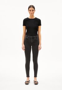 T-shirt noir à côtes associé à un jean foncé. Le jean est ajusté, avec une taille haute et une légère élasticité, complété par des chaussures à plateforme noires ouvertes à l'avant.