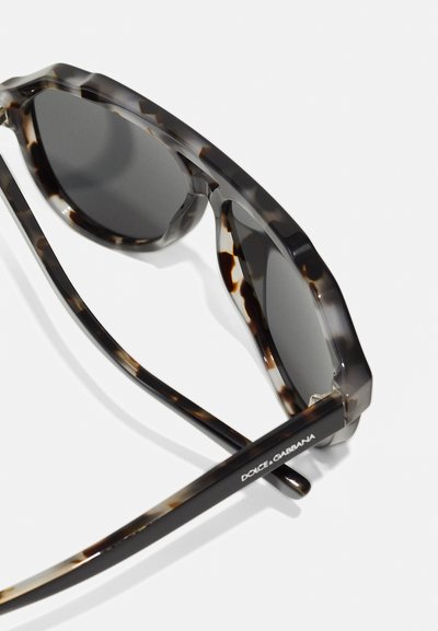 Ochelari de soare gri texturat cu lentile închise. Design cu ramă groasă și unghiulară. Prezintă un braț branduit cu o finisare netedă.