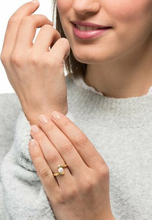 Goldring mit einem einzelnen Perlenakzent, an einer Hand getragen, mit einem glatten Band und minimalistischem Design, vor einem hellgrauen Pullover.