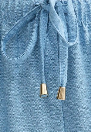 Close-up van blauw gestructureerde stof met een vastgeknoopt trekkoord met metalen gouden aglets aan de uiteinden.