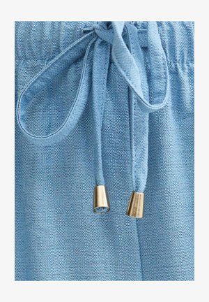 Close-up van blauw gestructureerde stof met een vastgeknoopt trekkoord met metalen gouden aglets aan de uiteinden.