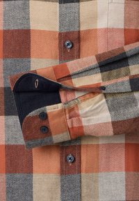 Flanellhemd mit großem orange-, beige- und grau-kariertem Muster, zeigt das Manschetten mit zwei schwarzen Knöpfen und kontrastierender dunkler Innenauskleidung.