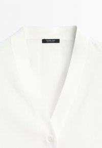 White garment with a deep V-neck collar and a black label reading Massimo Dutti Made in Portugal at the back inside collar.