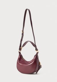 Sac à main en cuir rouge foncé en forme de croissant avec deux sangles réglables et des accents de fermeture éclair dorés sur un fond uni.