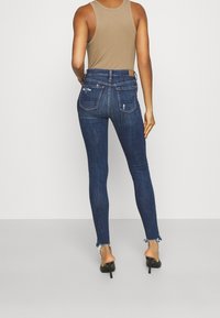 Smala jeans i mörkblå denim, med slitna detaljer och fransade kanter. Kombinerat med en tan ärmlös topp och svarta klackar.