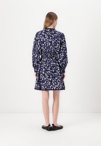 Blumenmusterkleid in Marineblau, mit langen Puffärmeln, einer taillierten Taille und einem gewellten Saum. Begleitet von schwarzen Slippers.