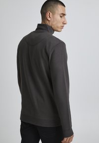 Felpa grigio carbone con collo alto, maniche lunghe e vestibilità morbida, caratterizzata da cuciture a vista e una texture soffice.