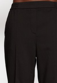 Pantalones negros con una textura suave, cintura elástica y detalle de bolsillos laterales. La tela parece ligera y resistente a las arrugas.