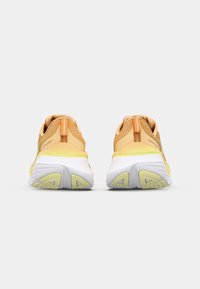 Deux chaussures de sport avec une tige en maille dégradée jaune à orange, une semelle intermédiaire blanche et une semelle extérieure en caoutchouc texturé. La vue arrière montre une languette pour un enfilage facile.
