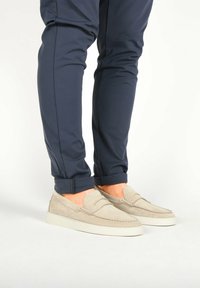 Beige semišové nazouvací boty s bílými gumovými podrážkami, s detailním prošíváním a hladkým povrchem, v kombinaci s námořnickými zúženými kalhotami.