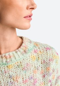 Pull en tricot pastel avec un col rond, motif texturé avec de petites formes colorées et une apparence douce et duveteuse.
