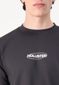 Fekete, rövidujjú pamut póló, elöl fehér "HOLLISTER" logóval. Sima tapintású, kerek nyakkivágású dizájn.