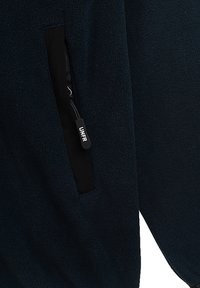 Tengerészeti fleece dzseki cipzáras zsebbel, textúrált felszínen és kontrasztos fekete részletekkel. A cipzáron található az "LNFR" márkajelzés.