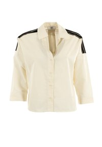 Camisa de botones color crema con mangas de tres cuartos, que presenta acentos negros en los hombros y un corte holgado. Fabricada con tejido ligero.