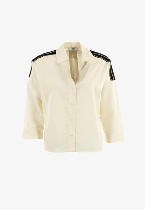 Camisa de botones color crema con mangas de tres cuartos, que presenta acentos negros en los hombros y un corte holgado. Fabricada con tejido ligero.