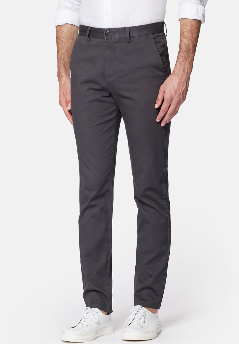 Szare bawełniane chinosy o slim fit, z przodem na guzik, bocznymi kieszeniami i gładką teksturą. Noszone z białymi trampkami.