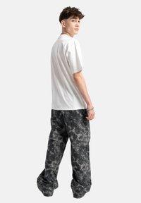 Biała bawełniana koszulka z krótkim rękawem w połączeniu z luźnymi spodniami cargo w szaro-czarny wzór. Materiał ma wyblakły, abstrakcyjny wzór.