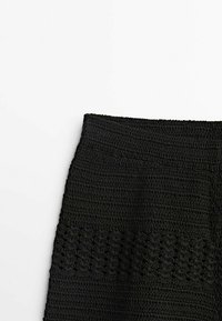 Jupe noire en crochet avec une bande texturée, présentant des motifs ajourés complexes dans la partie inférieure et un haut tissé lisse.