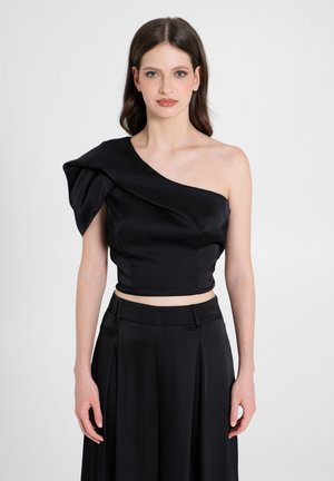 Schwarzes Crop-Top mit einem einseitigen Design, das mit drapiertem Stoff und glatter Textur versehen ist. Kombiniert mit einer hochgeschnittenen schwarzen Hose.