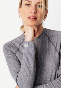 Top gris de manga larga con un tejido texturizado, cuello redondo y costuras en contraste. Pequeño logo bordado en el puño.