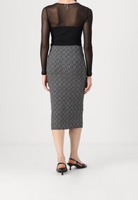 Haut à manches longues en mesh noir associé à une jupe moulante à motif géométrique noir et blanc, arrivant au genou. Des sandales à talons noires complètent le look.