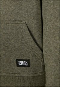 Felpa verde oliva con cappuccio caratterizzata da una tasca a marsupio, orlo e polsini a coste, e un'etichetta quadrata con "URBAN CLASSICS" in bianco e nero.