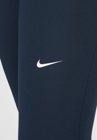 Marina blå träningsleggings i ett mjukt material, med en vit Nike-logotyp och en subtil sömdetalj längs sidan.