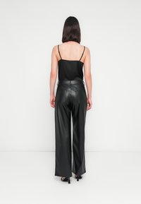 Camisole en satin noir avec des fines bretelles associé à un pantalon large en cuir noir taille haute, doté de poches et d'une texture lisse.