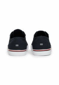 Zapatillas de lona marinas con suelas blancas, rayas rojas y blancas en la entresuela, y un pequeño logo en el talón. Diseño de perfil bajo.