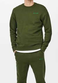 Bluza oliwkowa z okrągłym dekoltem, ściągaczami przy mankietach i u dołu, z małym zielonym logo na piersi. Miękki materiał o luźnym kroju.