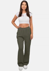 Olijfgroene, lichtgewicht geweven broeken met een elastische tailleband, taps toelopende pasvorm en textuur aan de oppervlakte. Gecombineerd met een witte crop top en sneakers.