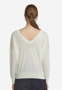 Leichter Pullover aus Creme mit V-Ausschnitt und geripptem Saum. Bietet einen lässigen Schnitt und lange Ärmel mit überschnittenen Schultern.