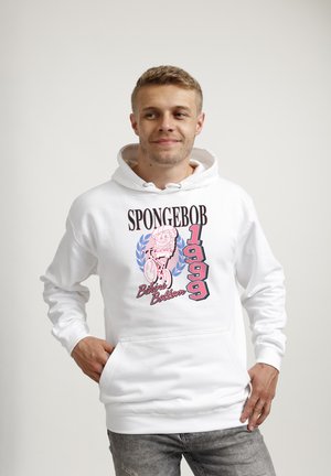Giovane uomo che indossa una felpa bianca con cappuccio con grafica rosa e blu di SpongeBob in bicicletta e testo "SPONGEBOB 1999 Bikini Bottom" sul davanti.