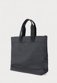 Čierna taška typu tote s textúrovaným povrchom, ktorý má opakovaný vzor loga. Má dve pevné horné rúčky a zapínanie na zips.