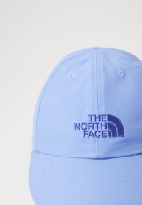 Világoskék, strukturált kialakítású textil sapka, elől egy lila hímzett logóval. A napellenző ívelt.