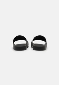 Svarta sandaler utan tår med två överdelar, platt gummisula, texturerad fotbädd och minimalistisk design.