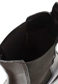 Black ankle boot featuring a textured leather exterior, elastic side panels, and a smooth, rounded toe. Interior lined with black fabric.