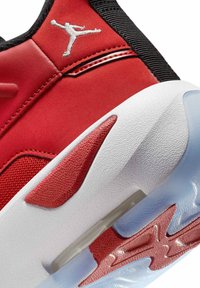 Czerwone buty sportowe z gładką zamszową cholewką, białą teksturowaną podeszwą, przezroczystymi niebieskimi akcentami oraz srebrnym logo po boku.