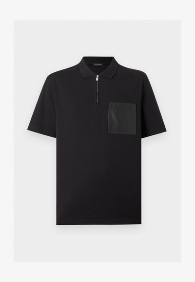 Μαύρο πόλο με κοντά μανίκια, κλείσιμο με φερμουάρ στη λαιμόκοψη και αντίθετη υφή τσέπης στο αριστερό στήθος.