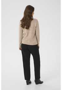 Beige knit sweater with horizontal cut-out details, paired with black trousers and black heeled ankle boots. Neutral colors and simple design.