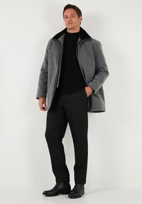 Chaqueta gris de mezcla de lana con cuello de piel negra, cierre de cremallera y dos bolsillos laterales, combinada con pantalones negros y botines.